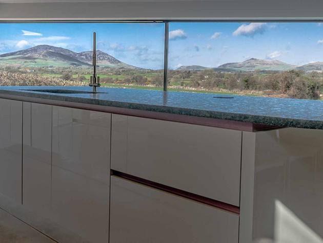 Kitchen extension featuring a Masterclass Kitchens white handleless gloss kitchen island and panoramic glass windows overlooking expansive landscape