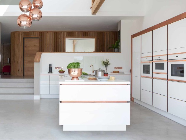 Kitchen extension in a converted open plan barn with timber beams white walls and Masterclass Kitchens white modern handleless cabinetry with metallic accents