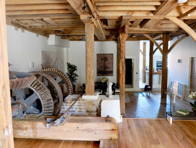 Open plan living area within a converted mill house featuring white walls timber beams exposed brick and a water wheel by Waterhouse Architects