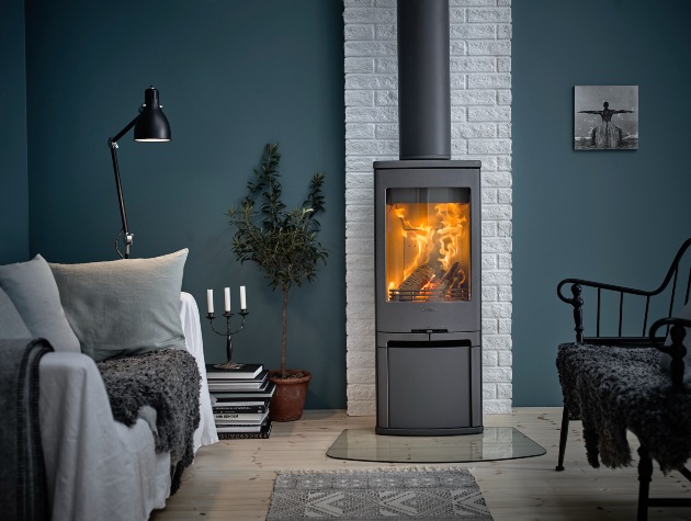 Modern lounge area with lit wood burning stove, sofa chair and dark painted walls