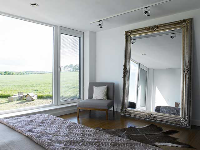 Bedroom overlooks garden with big wall to ceiling period mirror and chair in corner 