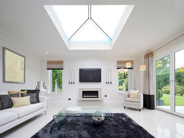 Interior of a contemporary living room with white walls and floors, a grey rug and aluminium roof lantern with LED lighting