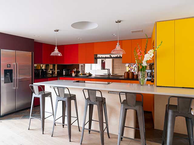 Vibrant kitchen in orange and yellow with breakfast bar inside Grand Designs Triangle house in Billingshurst