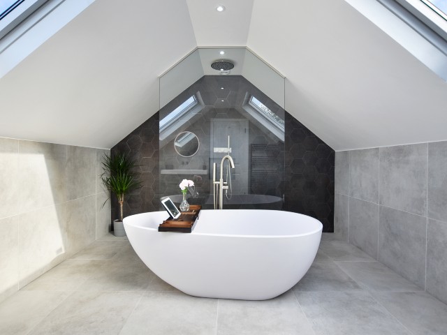 Interior of luxury attic bathroom with teardrop-shape freestanding bath, walk-in shower and dark bronze hexagonal tiled wall