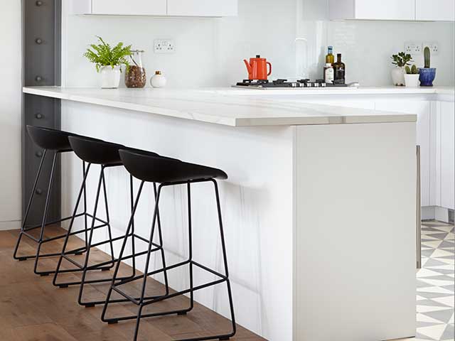 peninsula kitchen island with white marble work-surface and breakfast bar with black stools