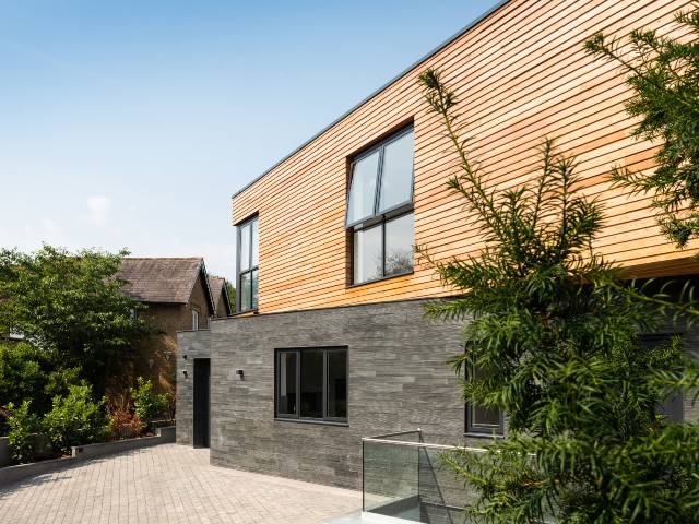 designing your eco home: timber and slate clad self-build house with large windows and lush green plants