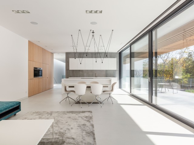 Interior of modern home with white open-plan minimalist kitchen and dining area and sliding triple-glazed doors 