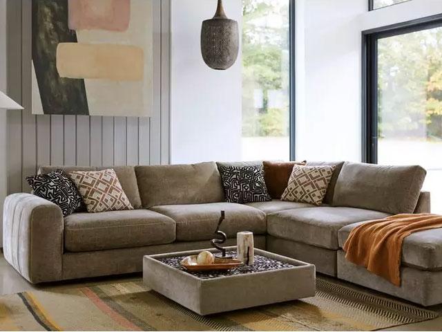 large taupe corner sofa with chunky arms and cushions and throws in brown, rust and orange