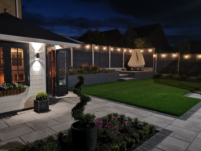 outdoor string lighting around the fence of a large garden with raised terrace 