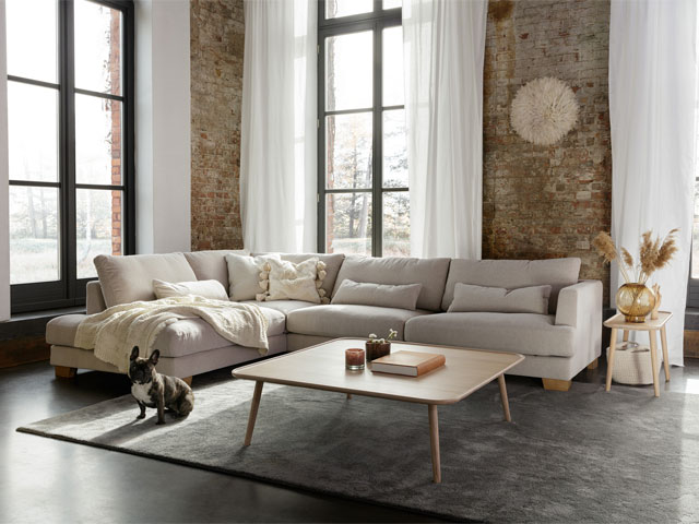large linen coach in a warehouse-style loft apartment with exposed bricks, large grey rug and french bulldog