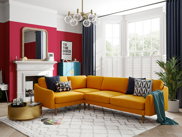 mustard yellow corner sofa in a period living room with large bay window and feature wall painted raspberry