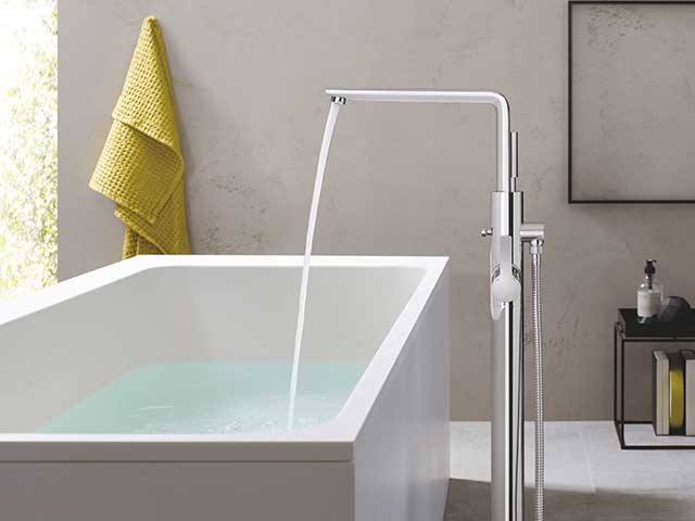 Silver tap poruing water into large square white basin, showers and taps