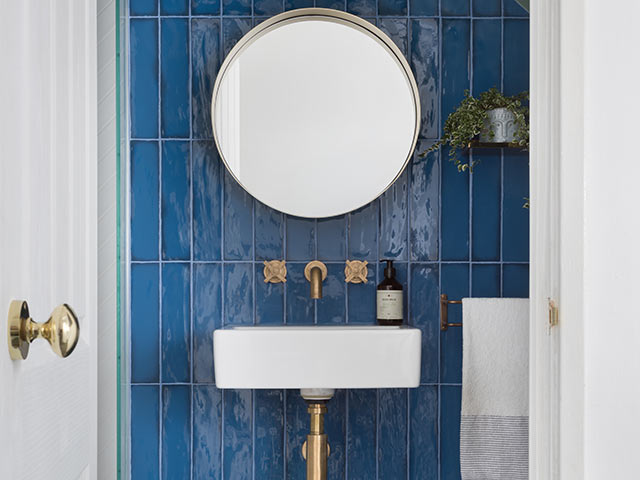 Blue tiled bathroom with white square basin and exposed brass pipes and taps