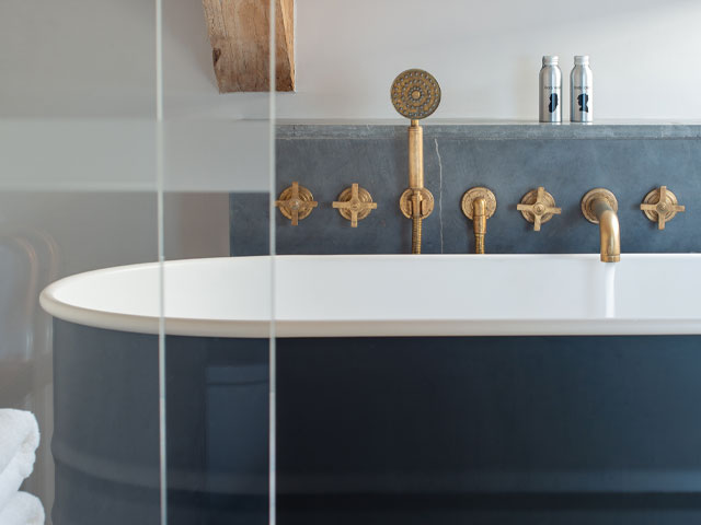 brass bath taps and shower head in an industrial chic decor scheme with navy painted bath