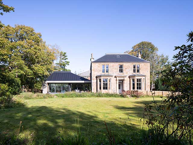 Scottish Victorian extension from outside grounds with trees and rural fields