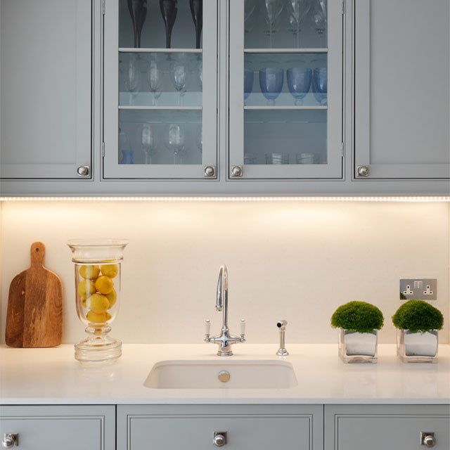 LED strip lighting under pale grey cabinets with white worktops and white sink