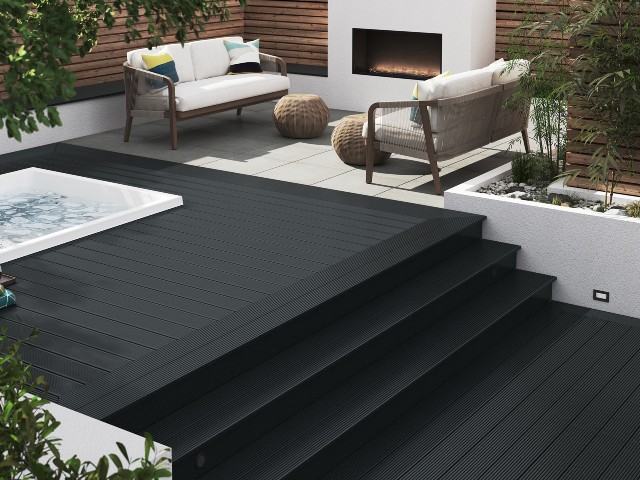 designer decking in black leading up steps to a raised terrace with a water feature and outdoor gas fire