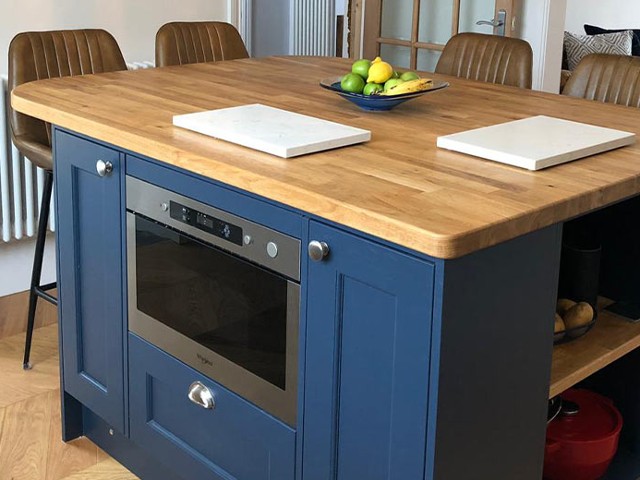 kitchen island with wooden worktop, blue painted cabinets, storage space and built-in microwave