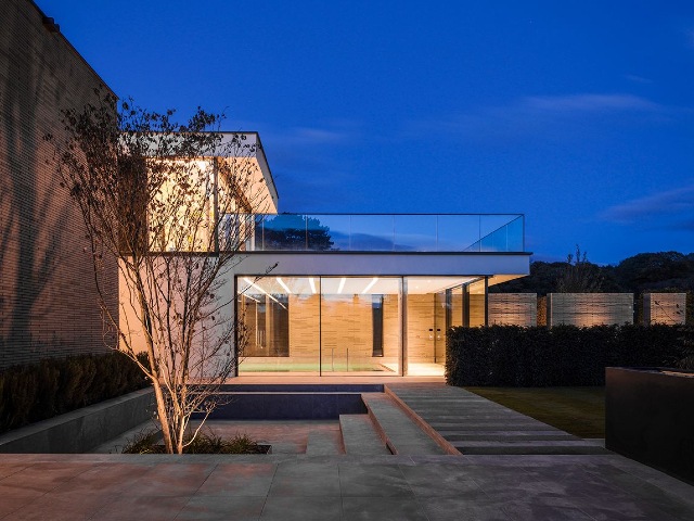 luxury home designed to blend into the landscape with large windows and lights on at night