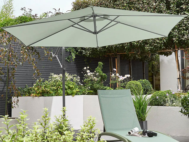 Pale sage cantilever parasol with grey stand over pale sage sun lounger in modern garden