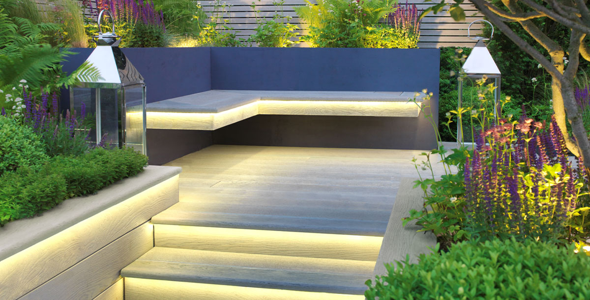 outdoor flooring ideas: decking with built-in lighting and bench seating in a raised corner of the garden
