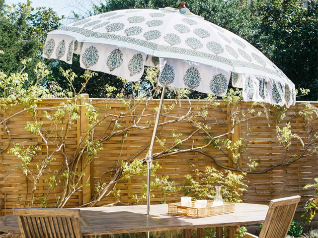 outdoor dining set with patterned umbrella with drinks tray next to a wooden fence