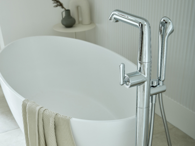 oval-shaped white freestanding bathtub with floor-mounted chrome tap and showerhead 