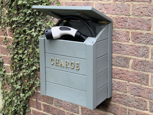 wooden electric car charging box on a brick wall with ivy growing up the wall