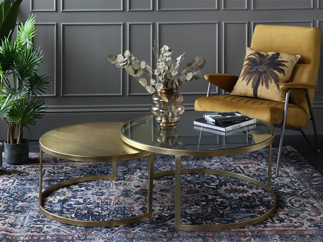 art deco style glass top nest of tables with gold legs on patterned rug with mustard chair