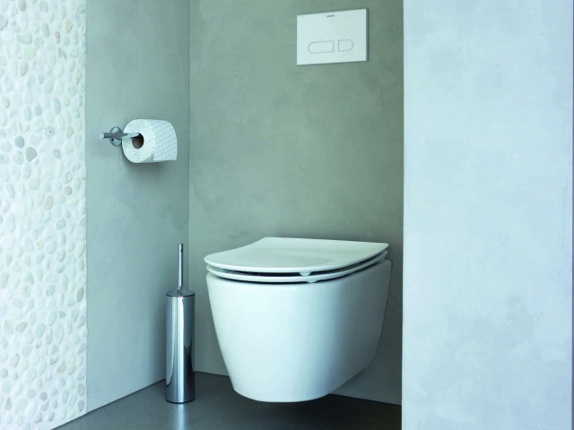 contemporary floating toilet in a bathroom with grey plaster walls and pebble-effect wall