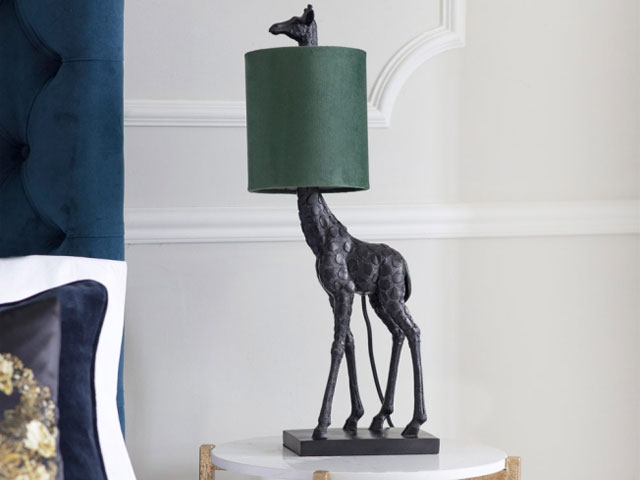 Giraffe lamp base with small green lampshade and giraffe's head sticking out of the top