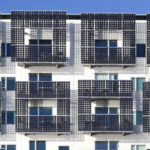 Contrasting black solar sells surround multiple balconies on a white building