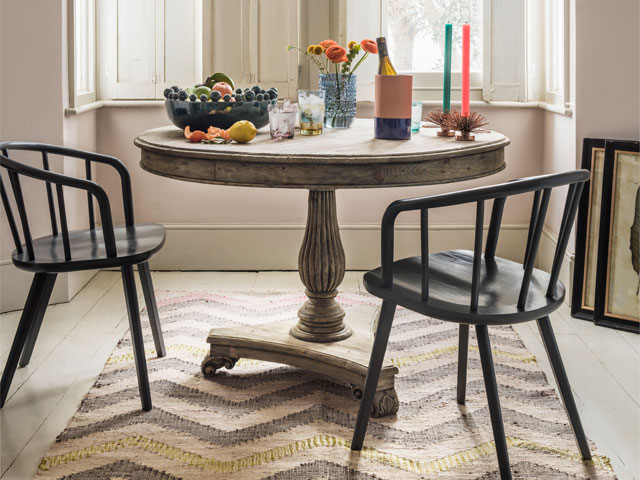 reclaimed round pine dining table with carved details in a bay window on a chevron rug