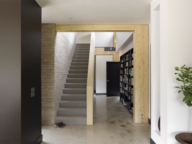 spacious hallway with large, black bookshelves, polished concrete floor and exposed bricks and timber beams