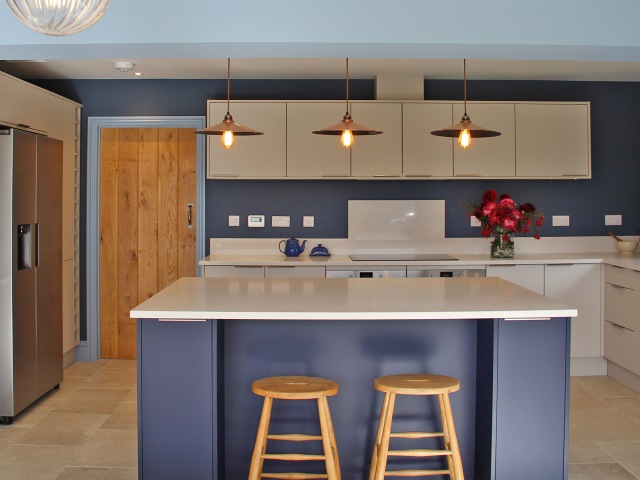 Modern kitchen with blue walls, white cupboards and a blue kitchen island in an old cottage