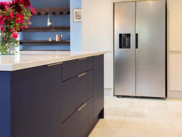 Modern kitchen with blue-painted island with deep drawers and big silver American-style fridge