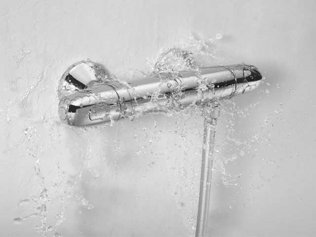 modern chrome shower tap splashed with water against a white wall
