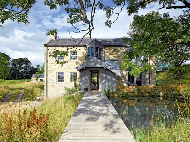 mill conversion in Northumberland with bridge over a lake leading to the front door