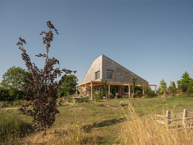 a timber frame eco home clad in western red cedar shingles with wrap-around terrace and surrounded by land