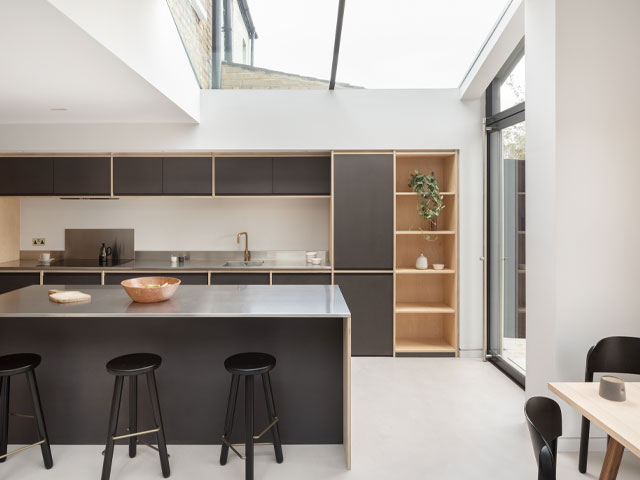A family home with side and rear extension to make space for a contemporary kitchen with dark grey cabinets, large island, overhead glazing and pivot door to the garden 