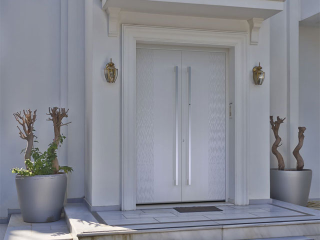 modern double front door with long silver bar handles on an old white building 