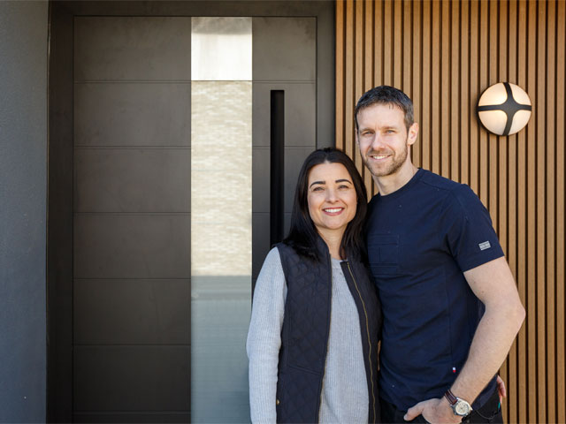 man and woman in front of contemporary house with black front door with wood panels