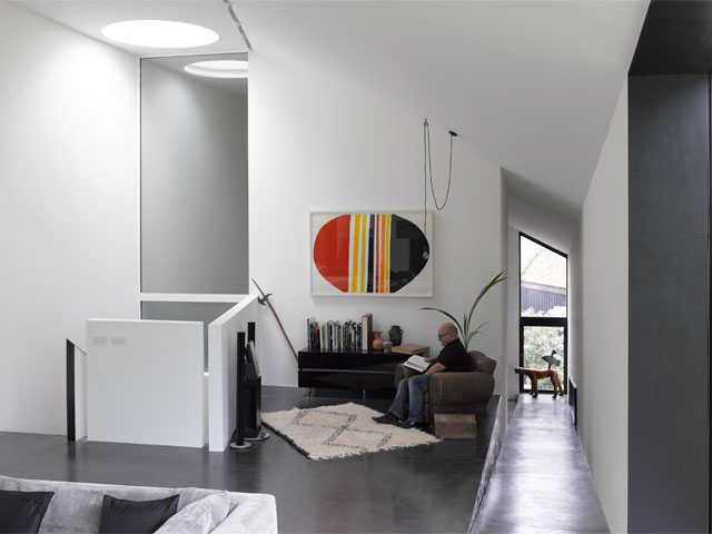 Man reading at reading nook in minimal contemporary home with concrete flooring and colourful artwork