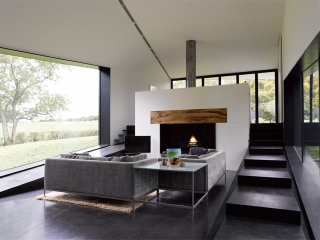 Concrete flooring in contemporary living room with grey furniture and open, centred fireplace in the Grand Designs Two Cocks Farm