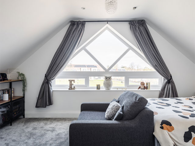 white painted bedroom with large triangular window blue sofa