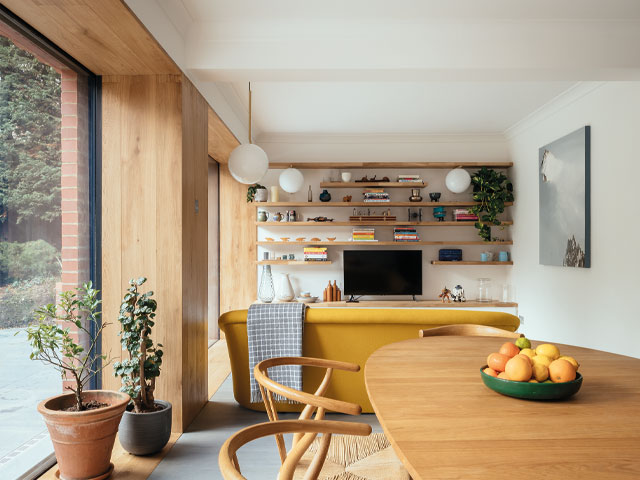 Open plan kitchen and living area oval dining table bright yellow sofa joinery shelving television plant pots