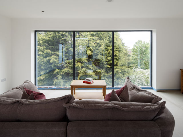 Grand Designs: The Streets. Large cushion sofa opposite large glazing large trees small wooden table