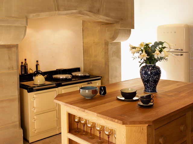 Grand Designs Hellifield Peel Castle. Stone alcove with Aga oven wooden table china vase flowers 