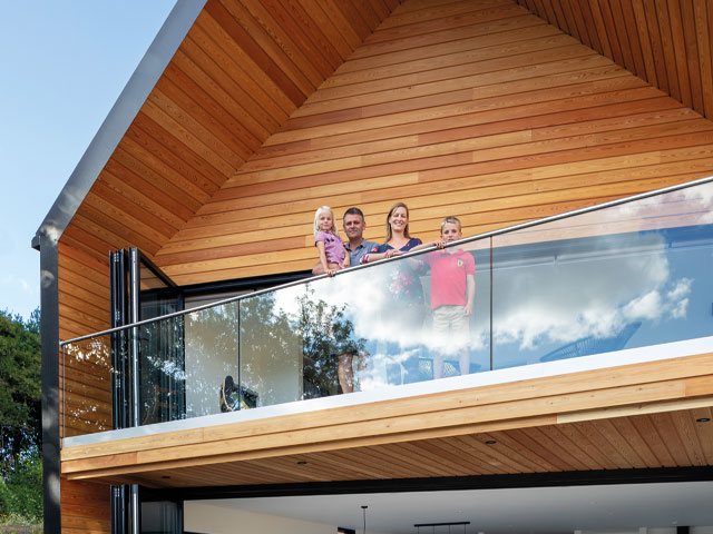 Grand Designs Leominster. Family on balcony with wooden cladding looking into camera