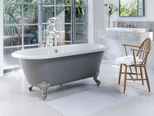 Double ended freestanding grey coloured bath white floor tiles white towel on wooden chair